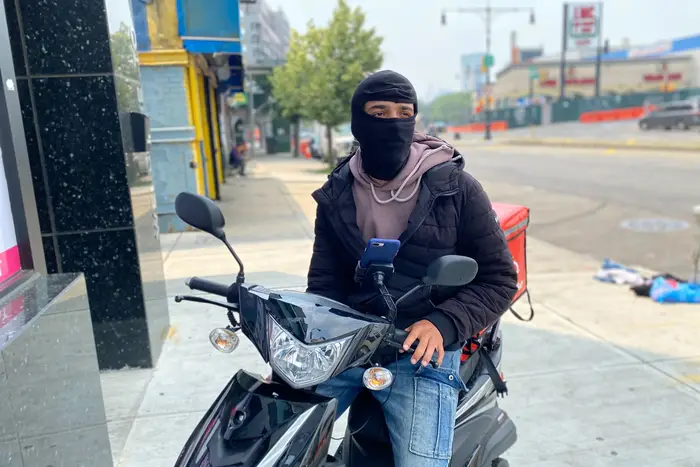 App-based food delivery worker Anthony Santillan sits on his motorcycle with a black face balaclava covering his face.